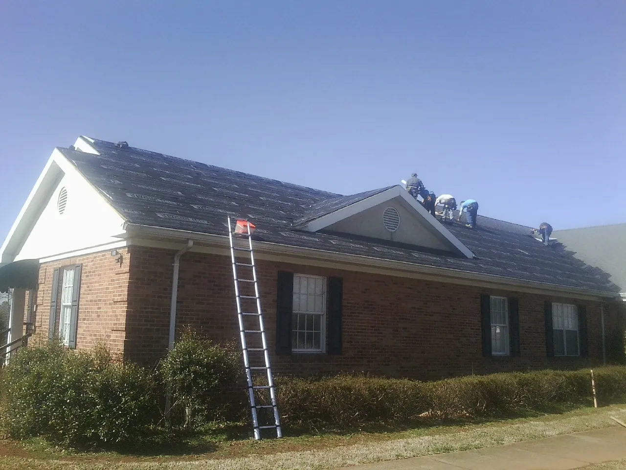 Crew tearing shingles off a brick ranch roof with a ladder set — Emergency Roof Repair work by our crew in Oldwick