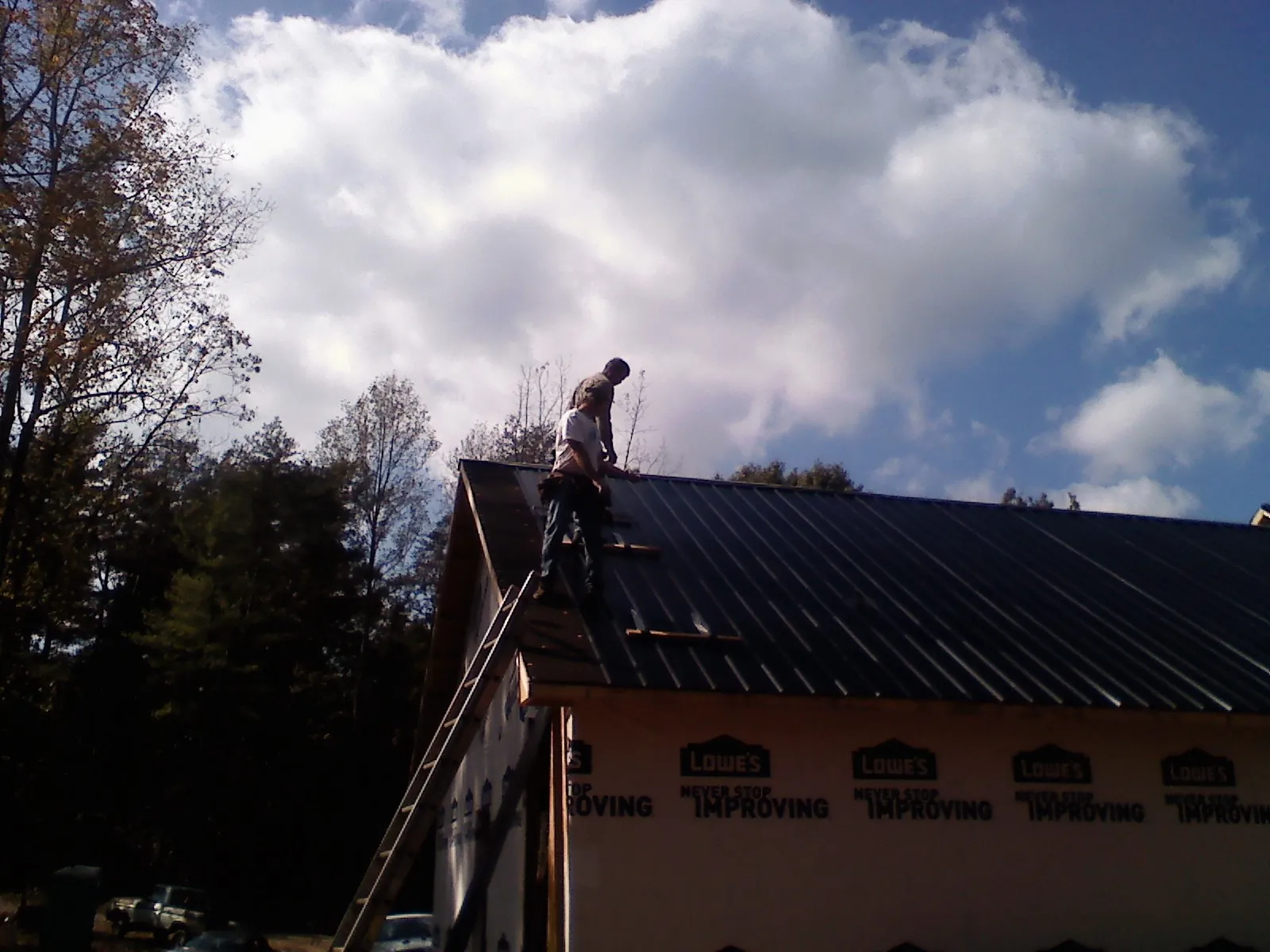 Roofer fastening dark metal panels high against a cloudy sky, from a Roof Inspection job in Oldwick